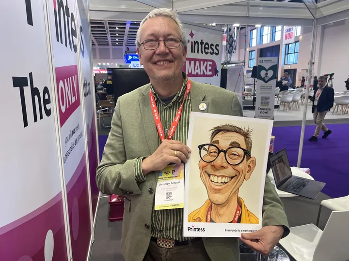 <p>Christoph Schacht på Printess under Fespa-mässan. Han håller upp en AI-genererad karikatyr av fotografen.</p>
